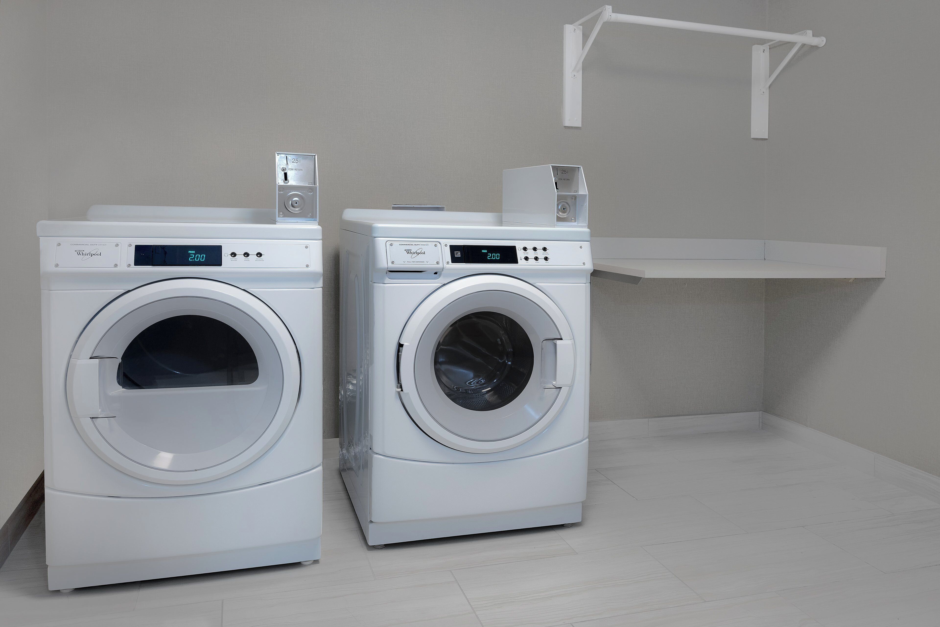 Two front-loading Whirlpool washers in a laundry room with a white shelf above.