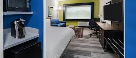 Habitación de hotel con cama, escritorio, computadora, microondas, cafetera y televisión.