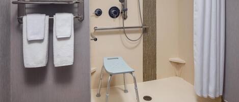 A bathroom with a shower, a towel rack with folded towels, a step stool, and a shower control panel.