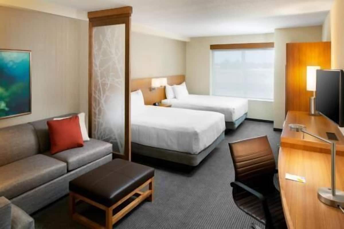 A hotel room with two beds, a sofa, a desk, and a TV.