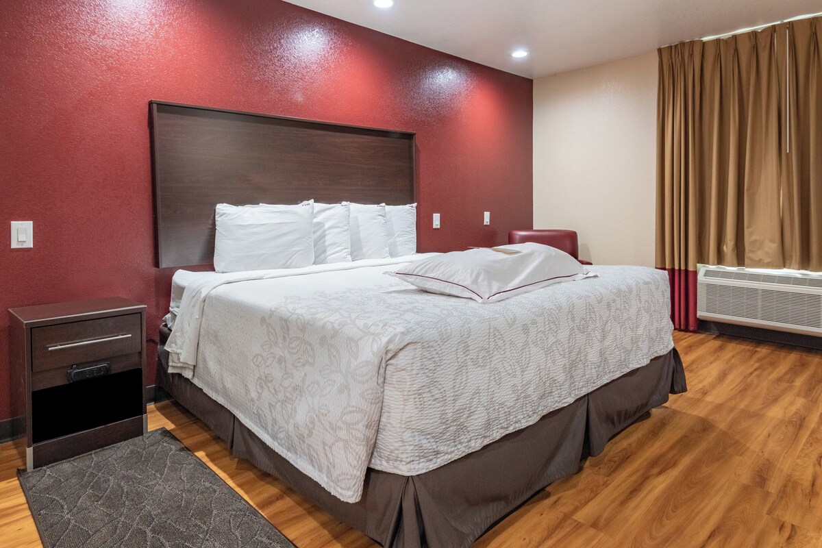 A hotel room with a large bed, a nightstand, a heater, and a window with curtains.