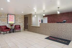 A reception area with a reception desk, two chairs, a wall-mounted sign, and a doormat.
