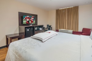 Habitación de hotel con cama, televisor montado en la pared, escritorio, silla y ventana con cortinas.