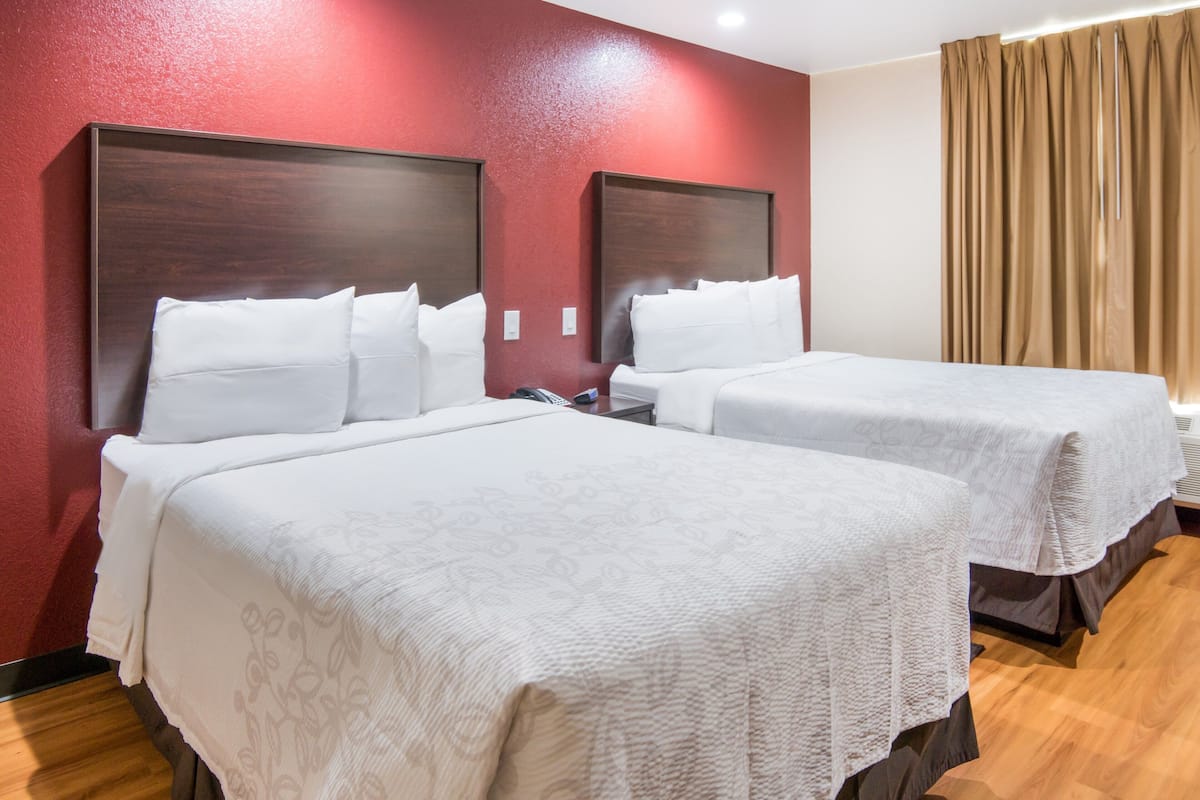 A hotel room with two beds, each with a wooden headboard, white bedding, and a red accent wall.