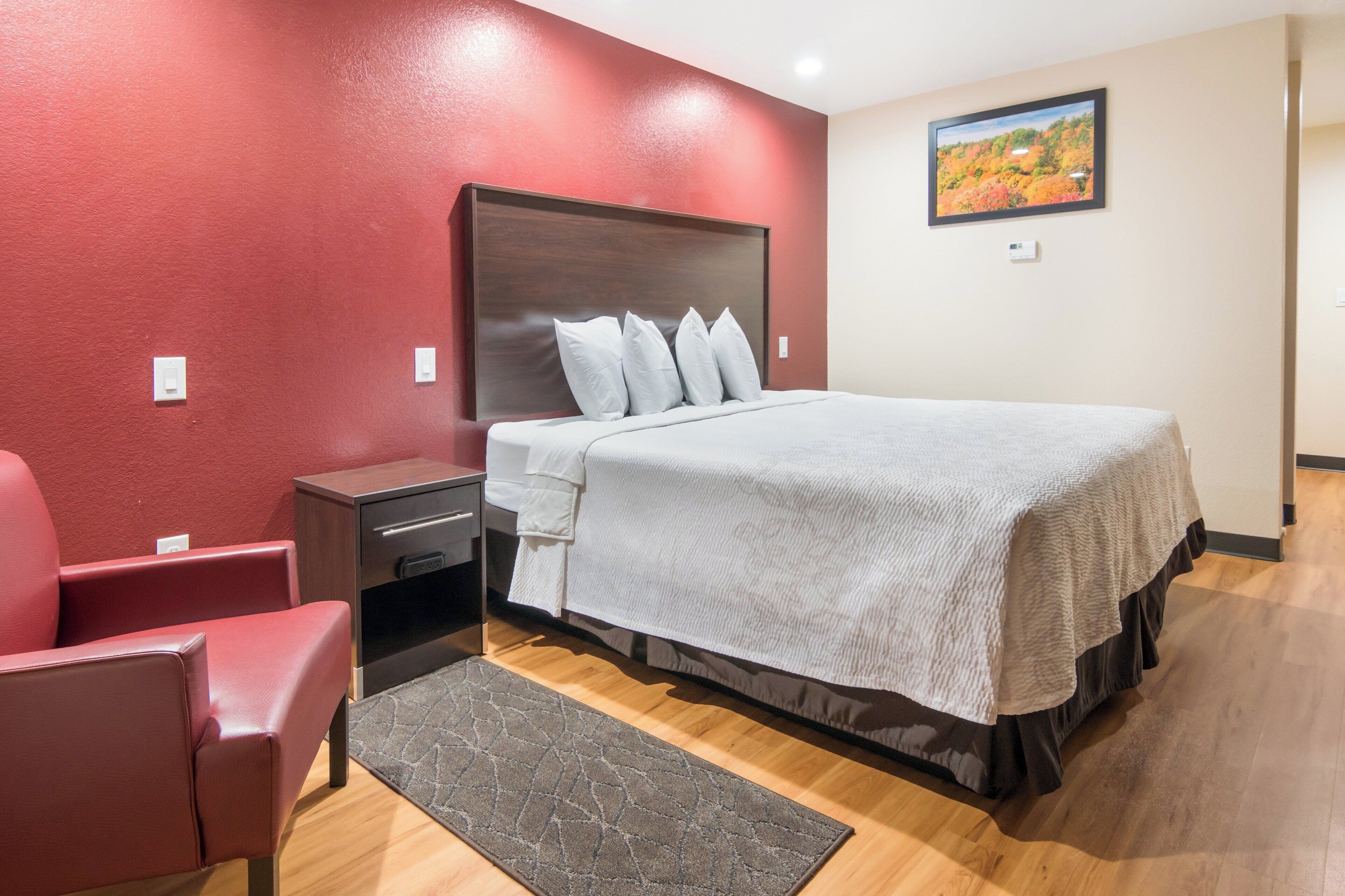 A hotel room with a bed, a nightstand, a chair, a rug, and a painting on the wall.
