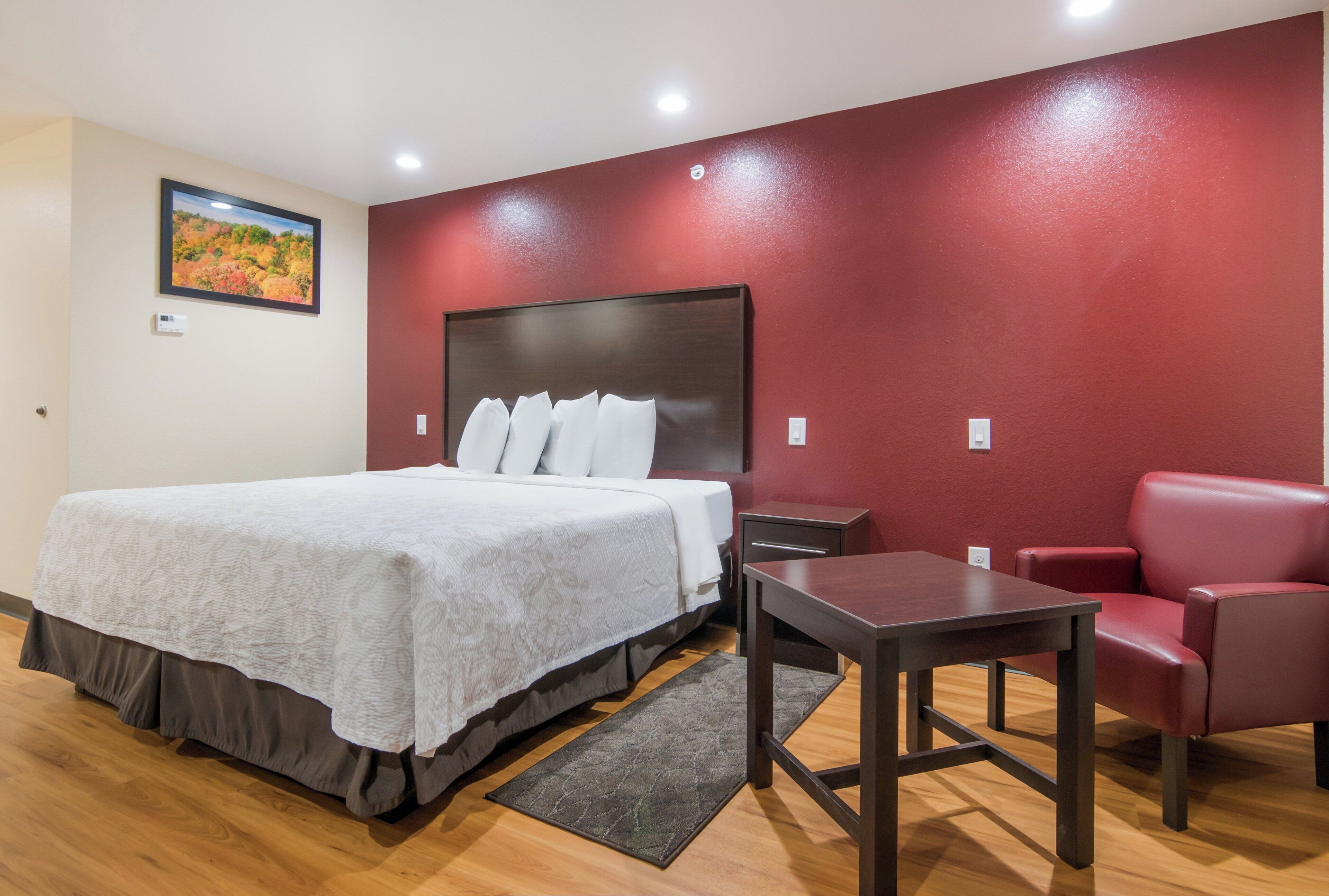Une chambre d’hôtel avec un lit, un bureau, une chaise et un mur d’accent de couleur rouge.