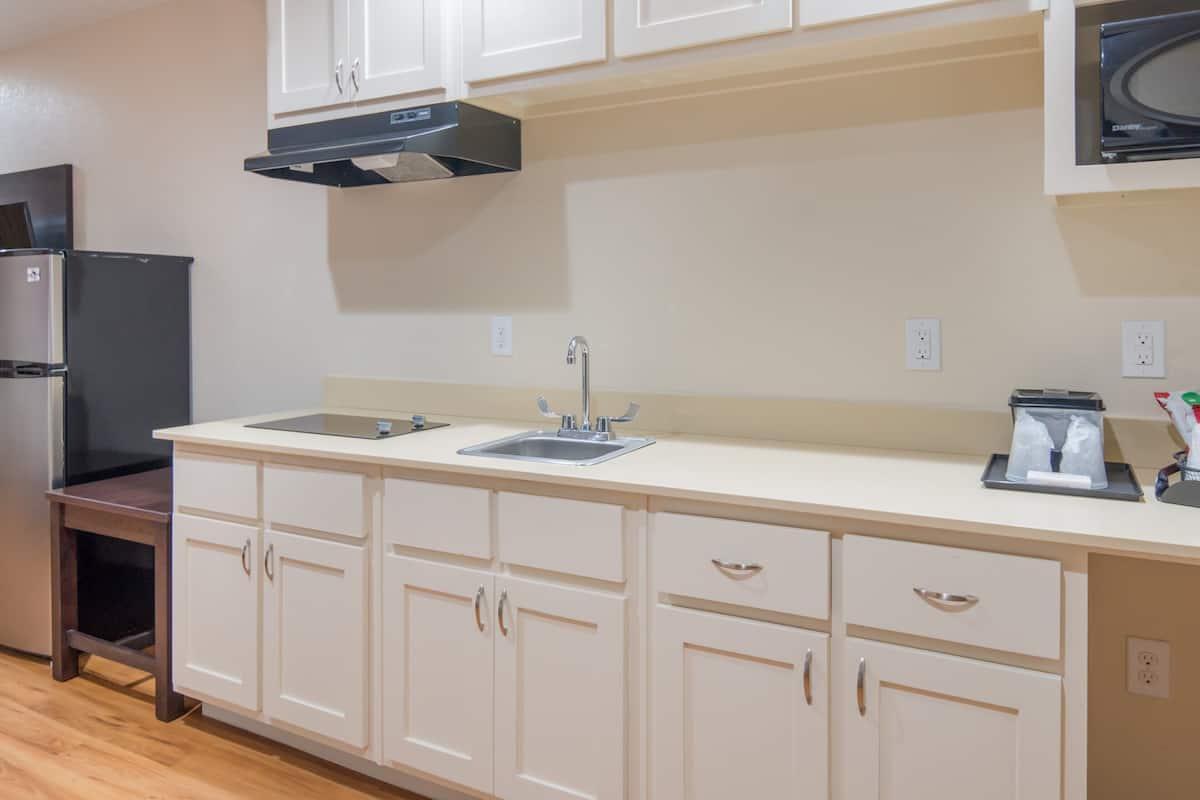 A kitchen with white cabinets, a black refrigerator, a stainless steel sink, and a microwave.