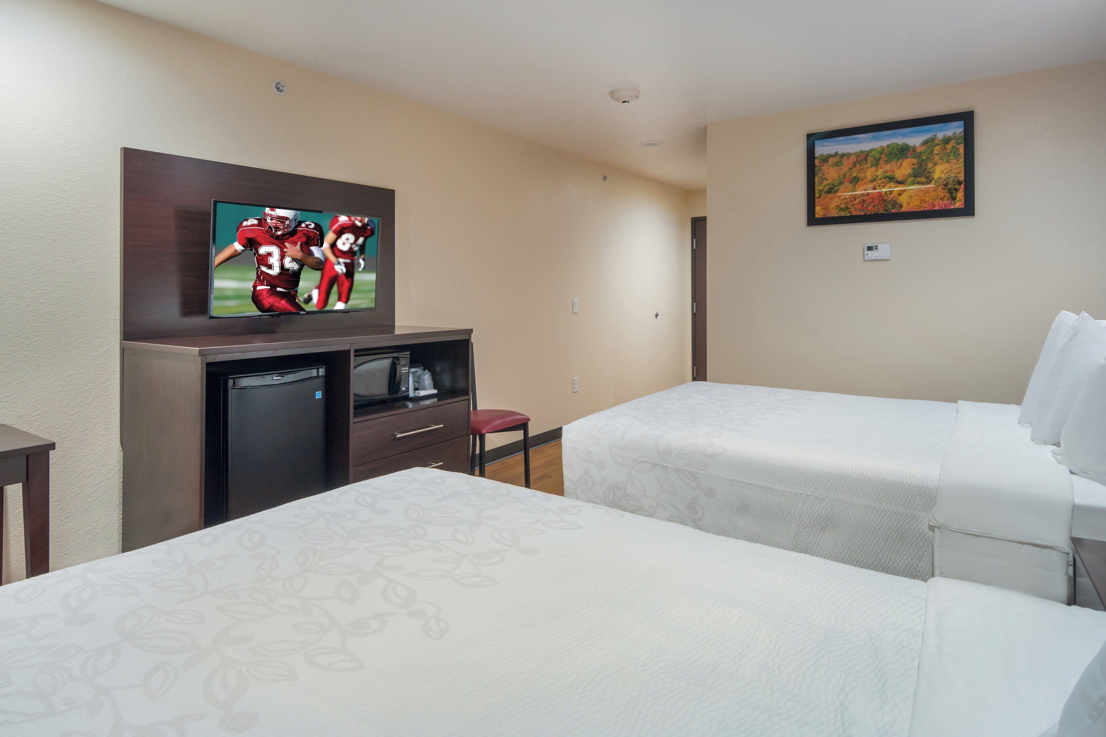 A hotel room with two beds, a TV, a small desk, and a painting on the wall.