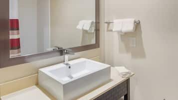 A bathroom with a white sink, a mirror, and two towels hanging on towel bars.