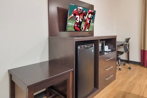 A compact hotel room with a flat-screen TV mounted on the wall, a small refrigerator, a desk, and a chair. - Red Roof Inn PLUS+ Fort Worth - Burleson (Burleson)