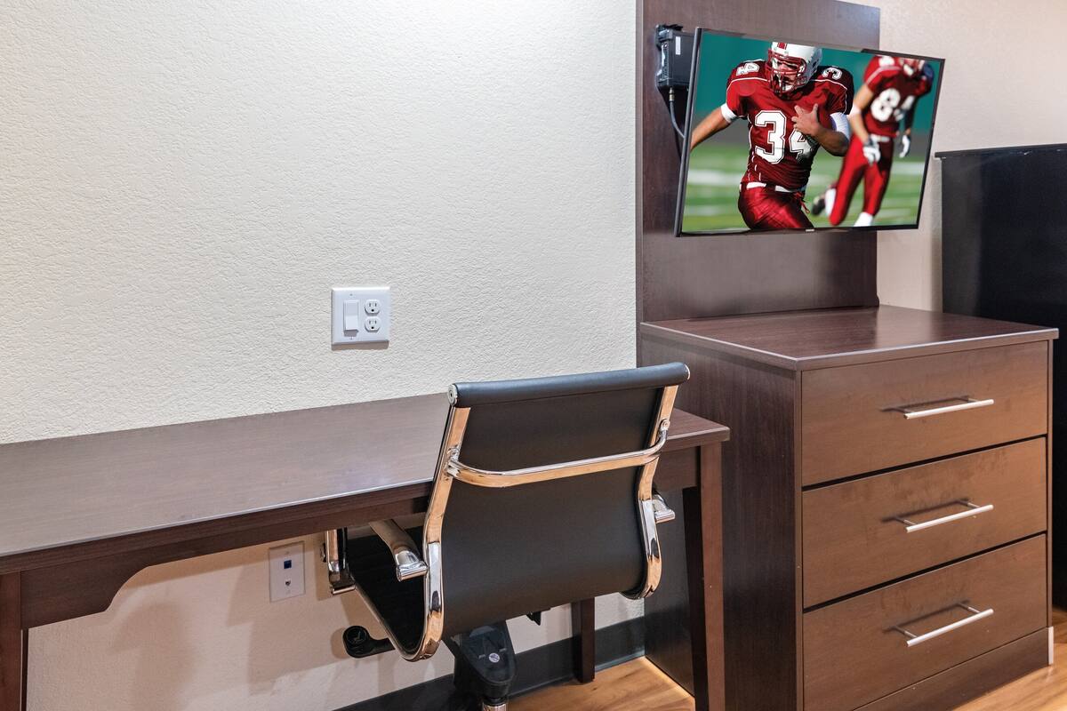 A modern room with a desk, a chair, a TV mounted on the wall, and a wooden cabinet.