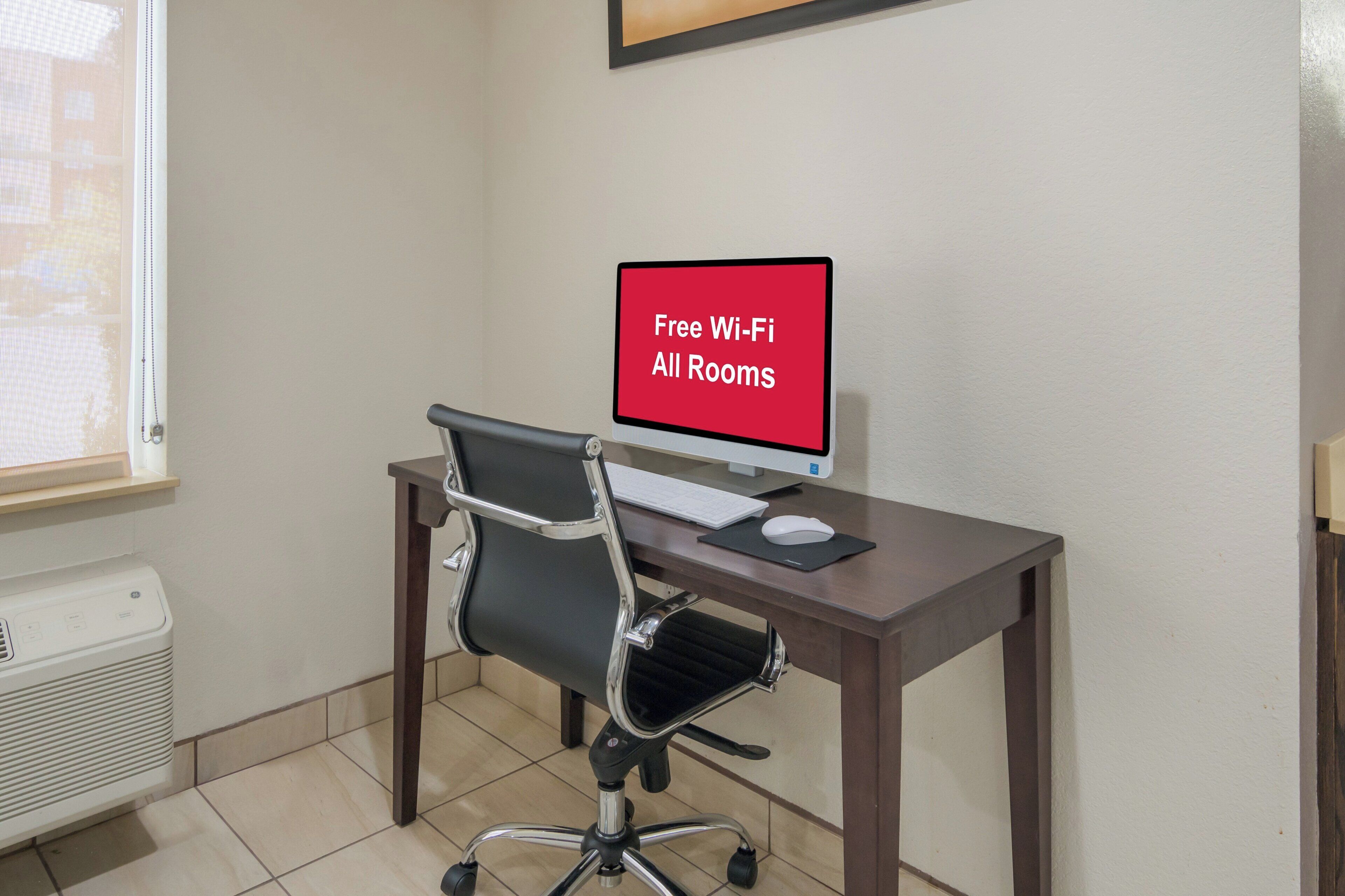 Una habitación con escritorio, silla, computadora y un cartel que indica Wi-Fi gratuito en todas las habitaciones.