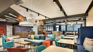 A modern lounge area with sofas, tables, and chairs, featuring a mix of seating arrangements and a central coffee station. - Tru by Hilton St. Charles St. Louis, MO (St. Charles)