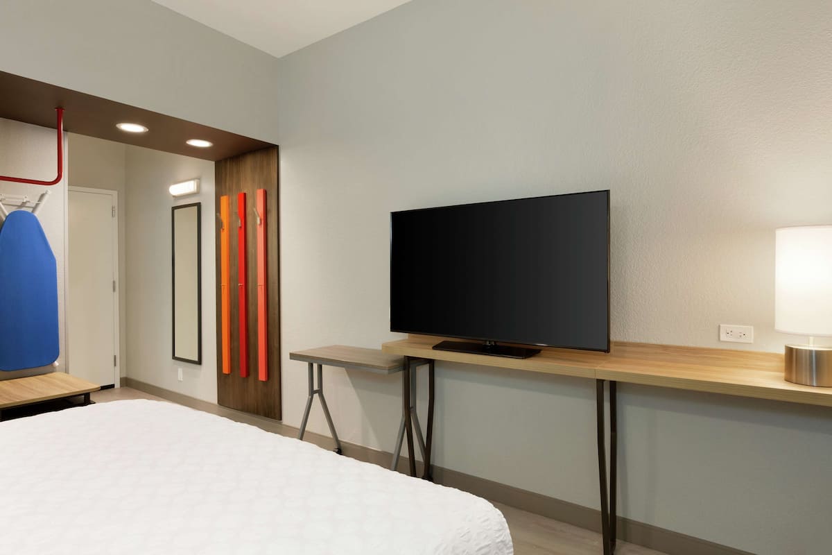 Una habitación de hotel con una cama, un televisor sobre un mueble de madera, una mesita y un espejo.