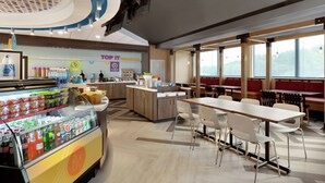 A modern cafe with a self-serve beverage station, a central island with seating, and large windows offering a view. - Tru by Hilton St. Charles St. Louis, MO (St. Charles)
