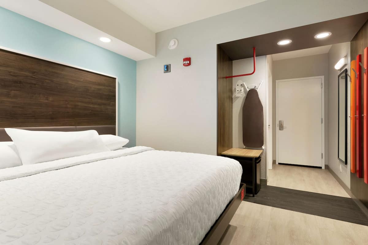 Habitación de hotel con una cama grande, un cabecero de madera, una mesita pequeña y una puerta que da a un baño.