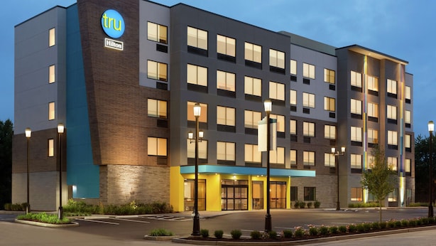 A modern hotel with a prominent Hilton logo, multiple floors, and a well-lit entrance. - Tru by Hilton St. Charles St. Louis, MO (St. Charles)