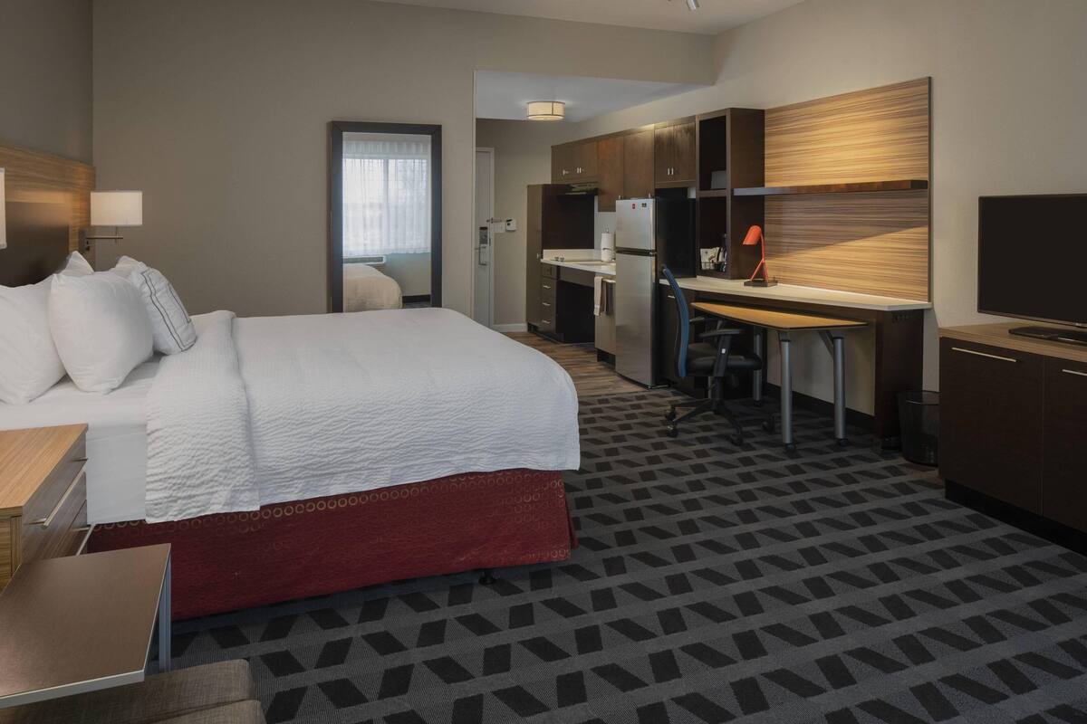Ein Hotelzimmer mit einem großen Bett, einem Schreibtisch, einer Küchenzeile und einem Fernseher.