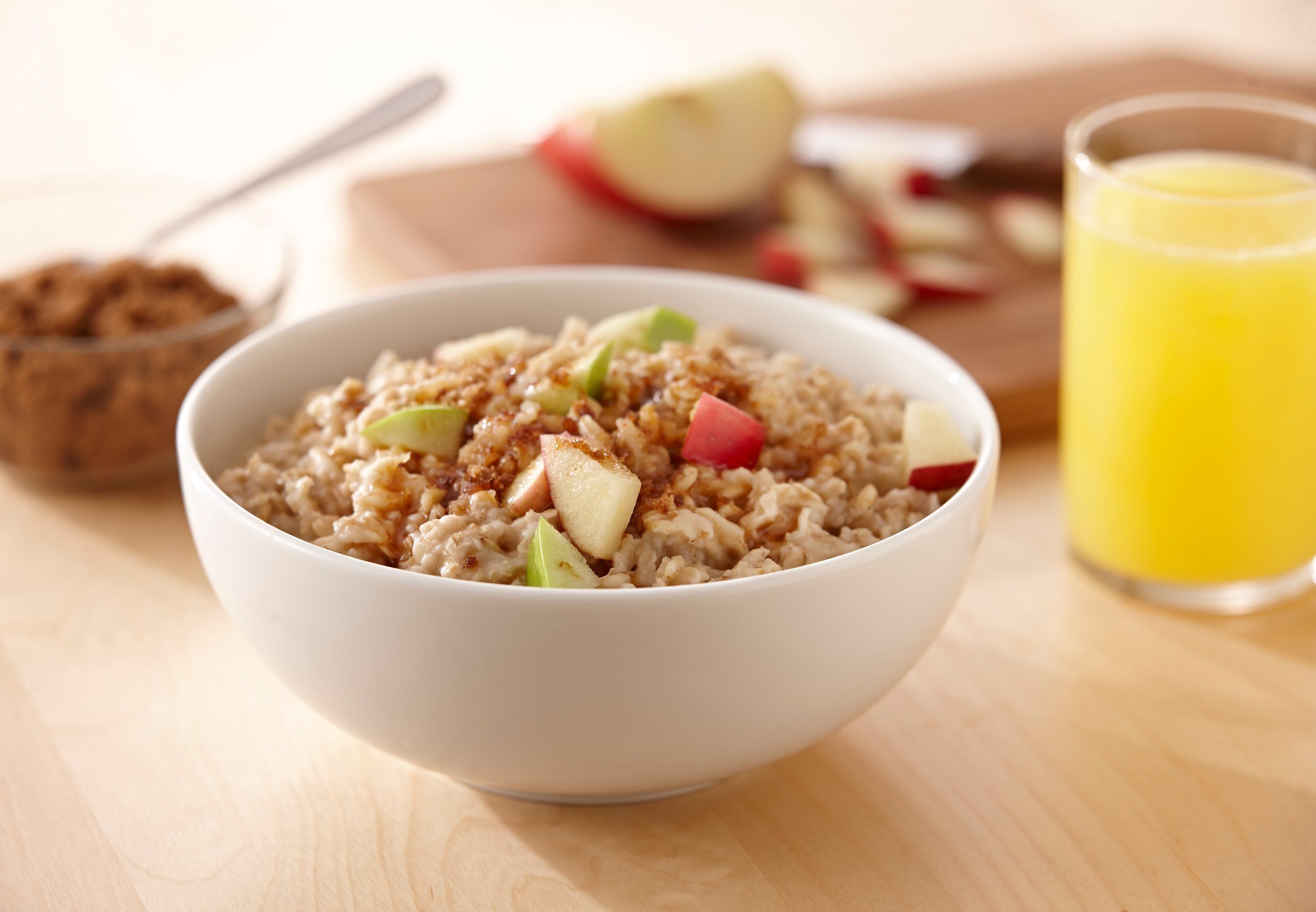 A bowl of oatmeal with diced apples and a glass of orange juice on a wooden table.