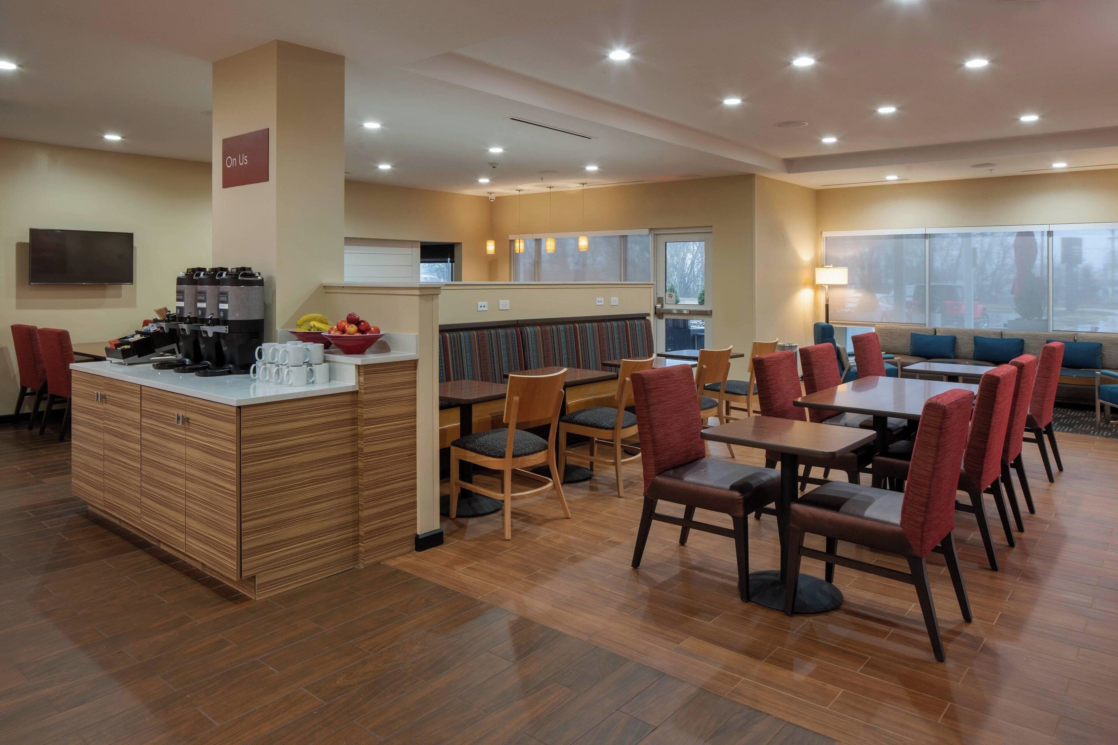 A modern hotel dining area with wooden flooring, a central bar, and seating arrangements.