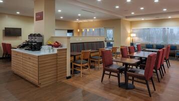 A modern hotel dining area with wooden flooring, a central bar, and seating arrangements.