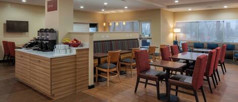 A modern hotel dining area with wooden flooring, a central bar, and seating arrangements.