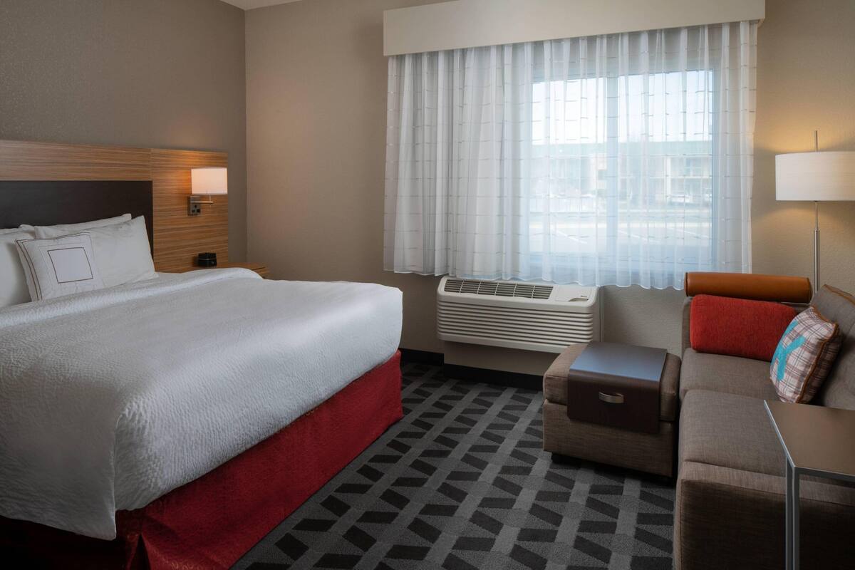Ein Hotelzimmer mit einem großen Bett, einer Couch, einem kleinen Tisch und einem Fenster mit Vorhängen.