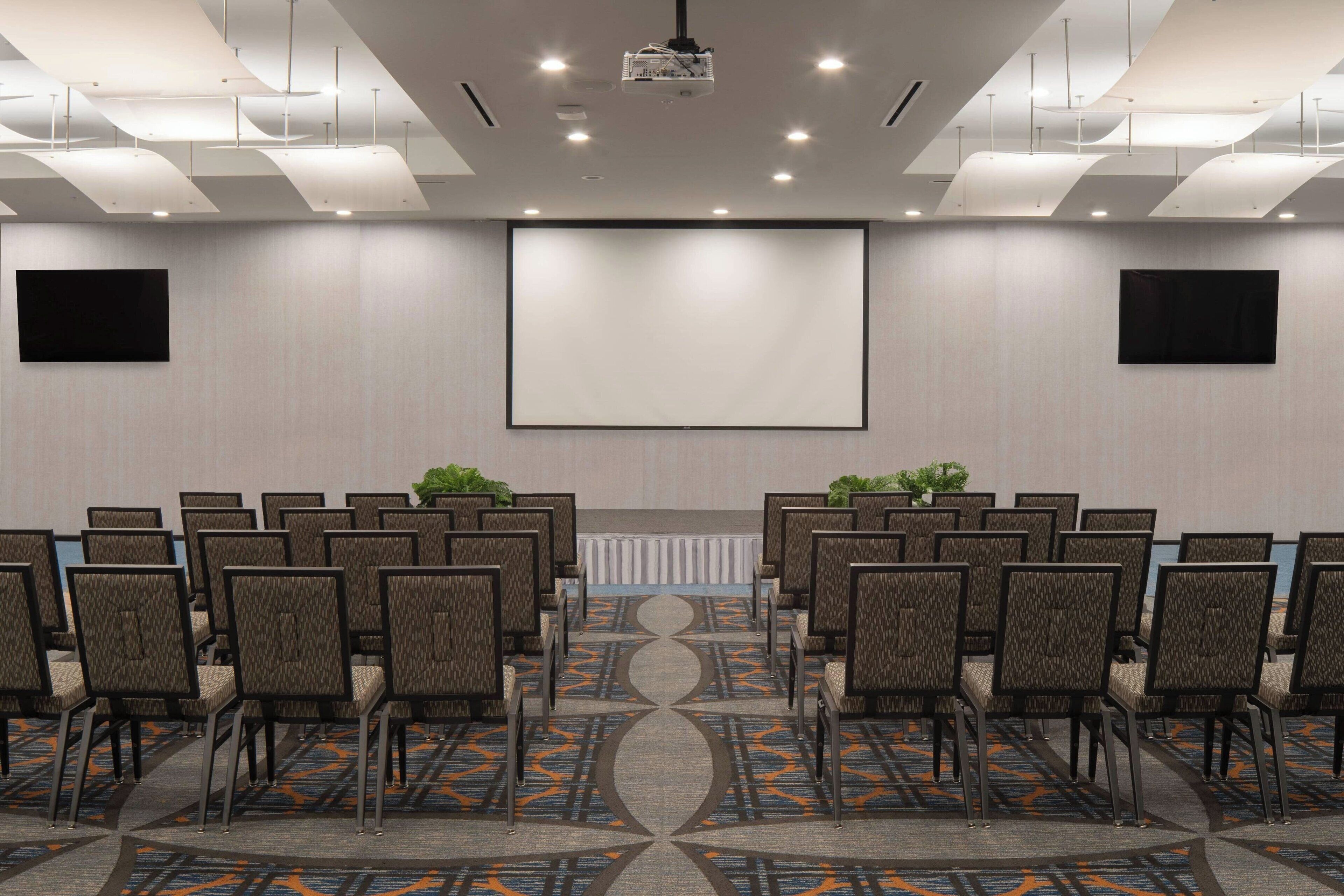 A conference room with rows of chairs, a large screen, and a projector.