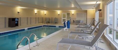 Una piscina interior con sillas de descanso, vestuario y vistas al exterior.