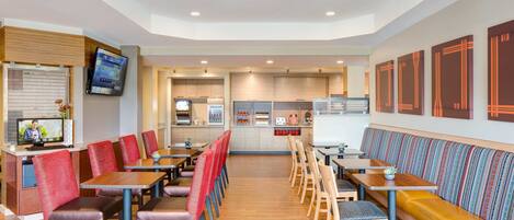 A modern restaurant with multiple seating areas, including booths and tables, and a counter with a television.