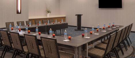 A conference room with a long table, chairs, water bottles, apples, and a TV screen.
