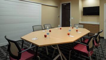 A conference room with a large table, chairs, water bottles, apples, and a TV on the wall.