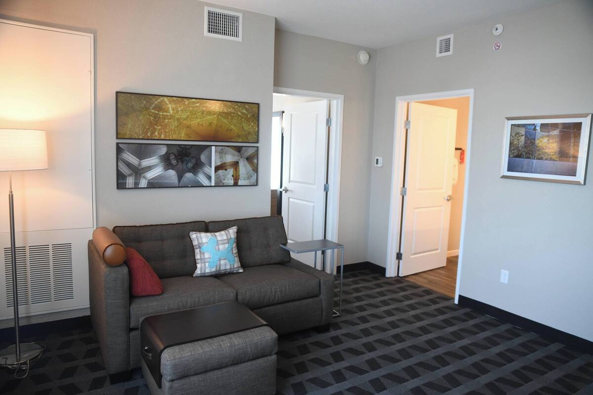 A living room with a sectional sofa, a small side table, and a lamp. There are two doors leading to other rooms.