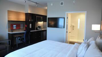 A hotel room with a bed, a desk with a chair, a microwave, a TV, and a door leading to a bathroom.