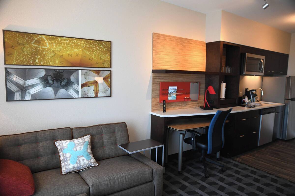 A modern living room with a grey sofa, a small table, and a kitchen area with a microwave and a red cabinet.