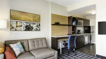 Habitación de hotel moderna con sofá, escritorio, silla, microondas, refrigerador y televisión de pantalla plana.