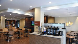 Un café moderne avec un comptoir, un espace salon et un écran de télévision diffusant le message « Nous vous offrons ».