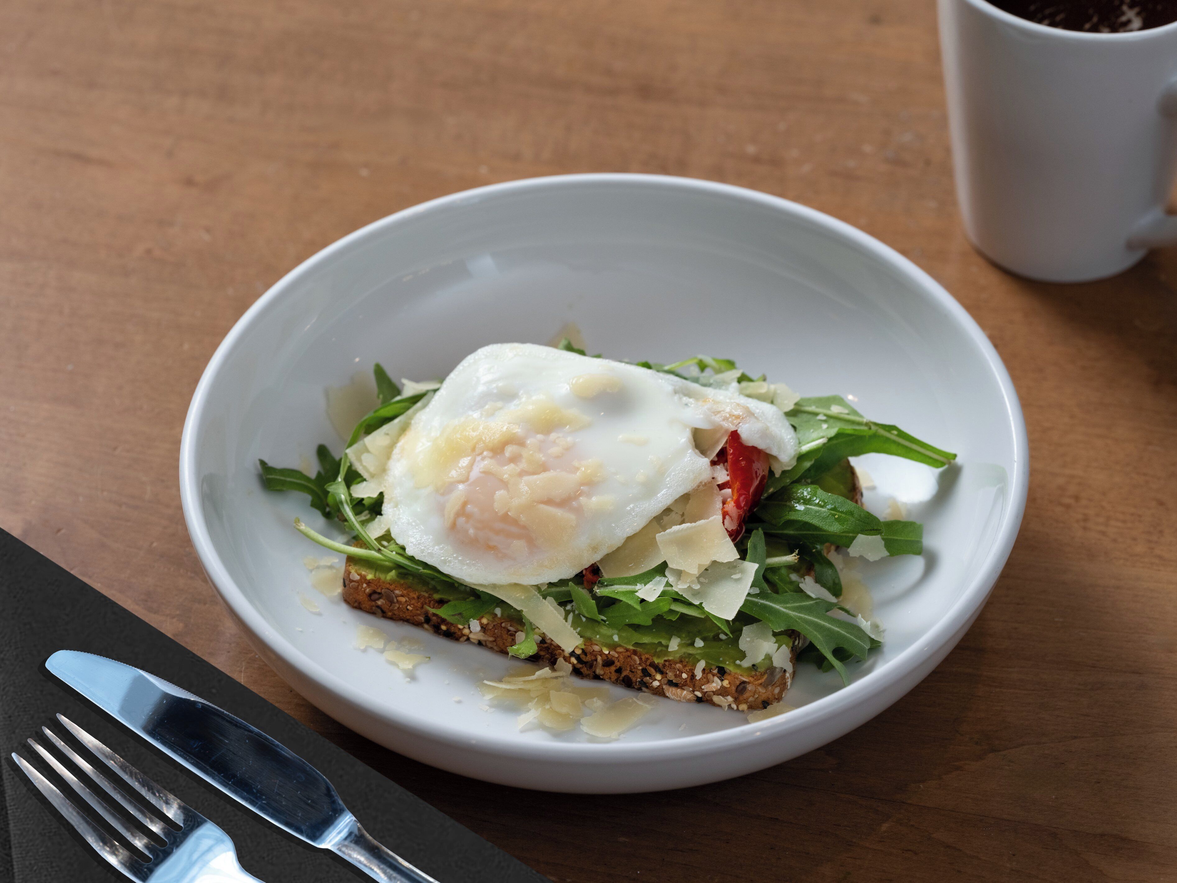 A white bowl with a breakfast dish, a fork, and a knife on a wooden table.
