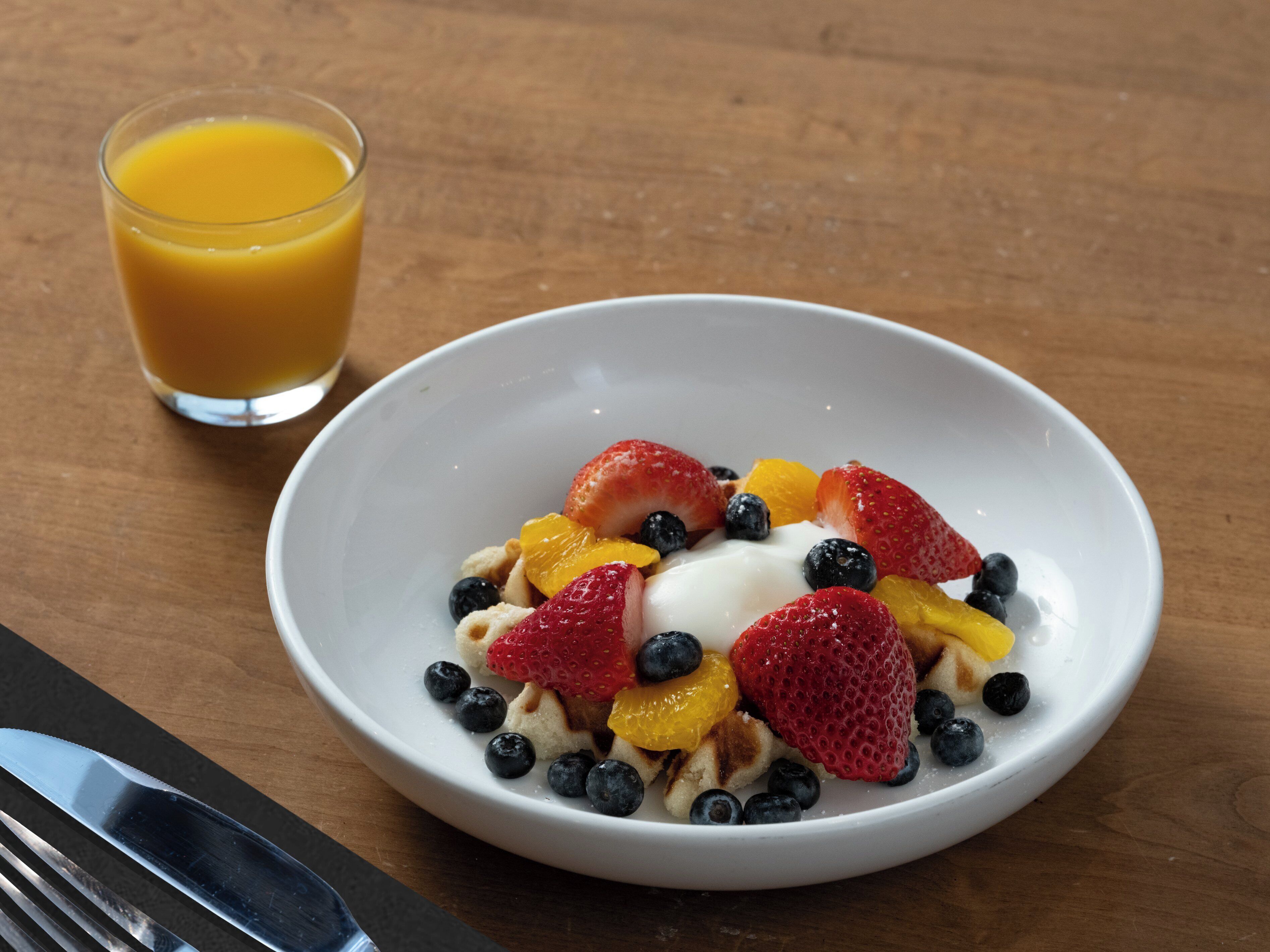 Un bol de cereals amb fruites i un got de suc d'aranja sobre una taula de fusta.