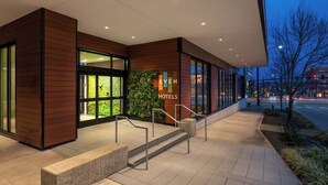 A modern hotel entrance with a glass facade, a wooden exterior, and a landscaped area with steps leading to the entrance.