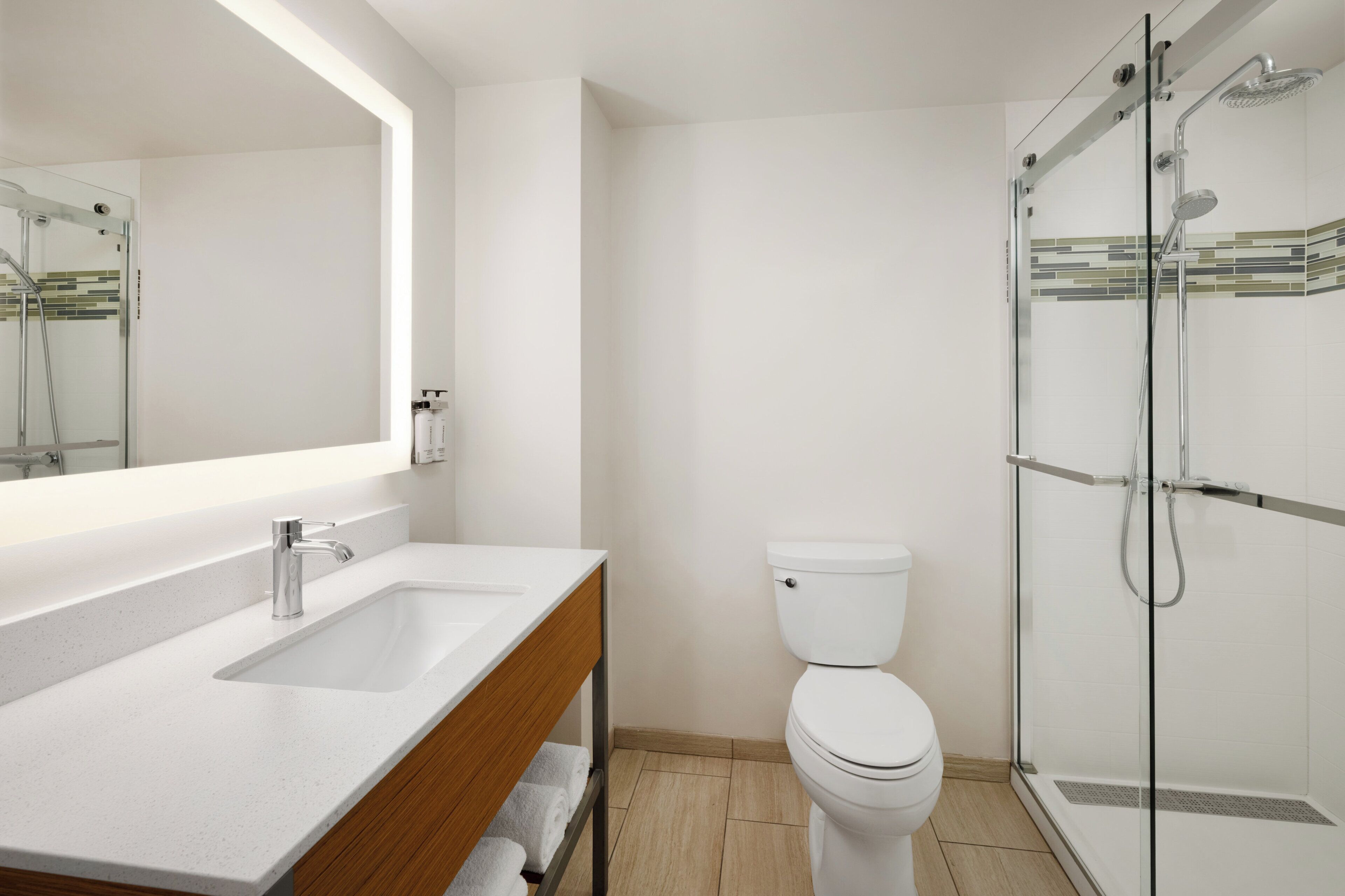 A modern bathroom with a glass shower enclosure, a white sink with a wooden vanity, and a toilet.