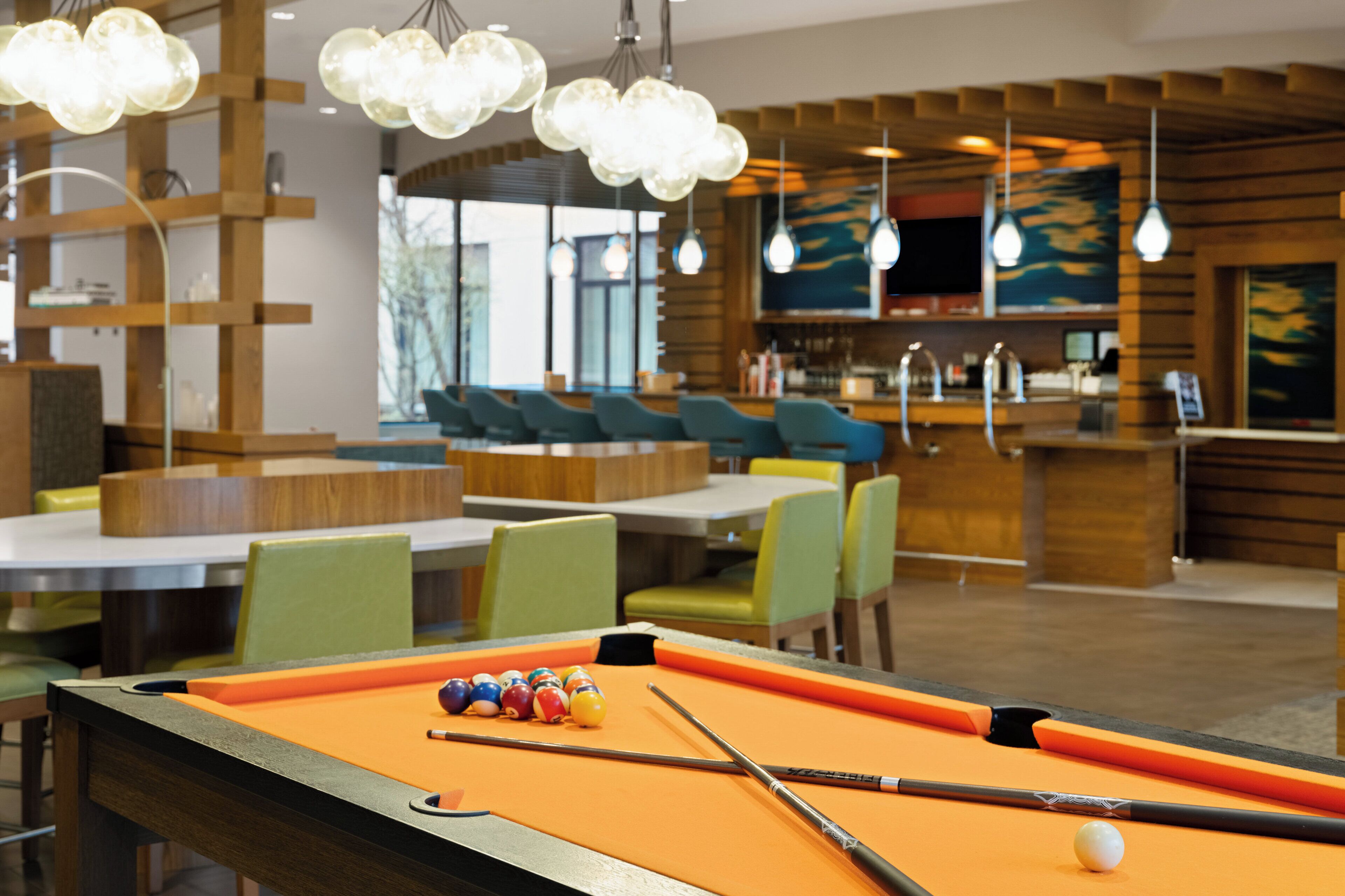 A pool table with balls and cues, wooden furniture, and hanging lights in a room with a bar area.