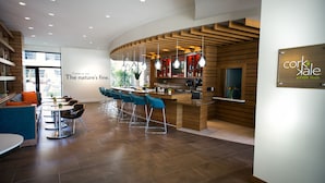 A modern hotel lobby with a curved bar area, seating with blue chairs, and a sign reading "cork & dale at EVEN Hotels".