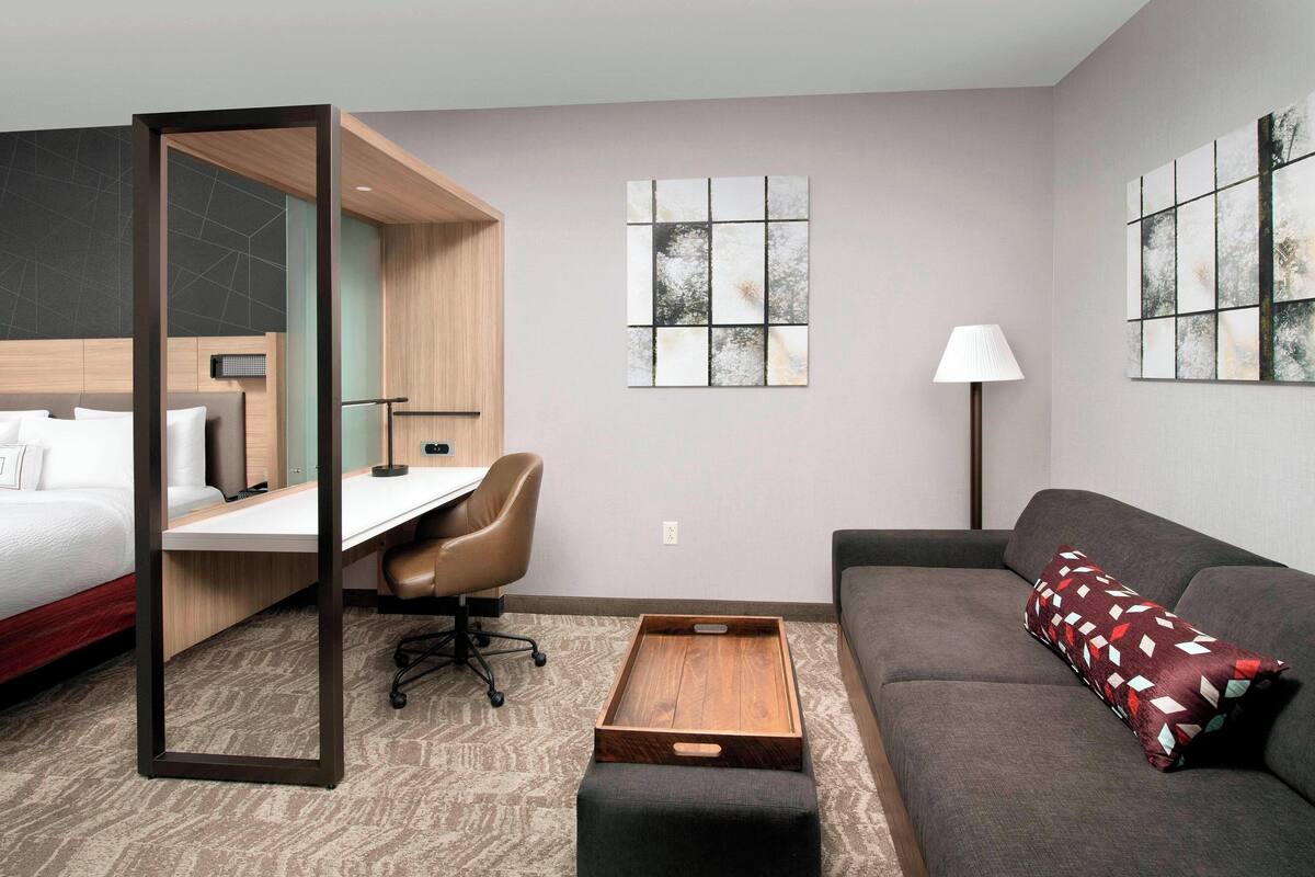 A hotel room with a bed, desk, chair, sofa, and artwork on the walls.