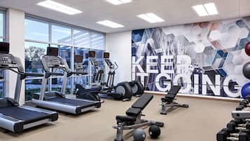 A gym with treadmills, elliptical machines, a bench, and dumbbells.