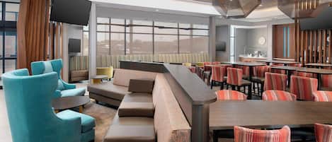 A modern hotel lobby with a seating area, a bar, and a large TV screen.