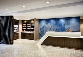 Un área de recepción moderna con una mesa de recepción, una estantería y una pared con diseños geométricos.