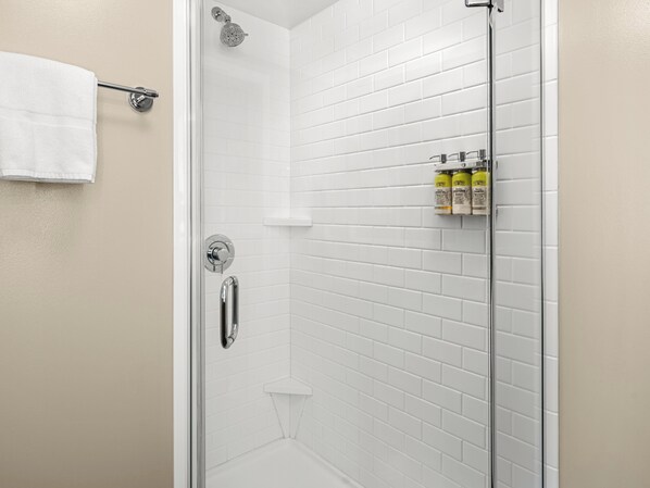 A glass-enclosed shower with white tiles, a towel rack, and a shelf with toiletries. - Staybridge Suites Seattle Downtown - Lake Union by IHG (Seattle)
