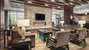 A modern living room with a stone wall, fireplace, comfortable seating, and a flat-screen TV. - Staybridge Suites Seattle Downtown - Lake Union by IHG (Seattle)
