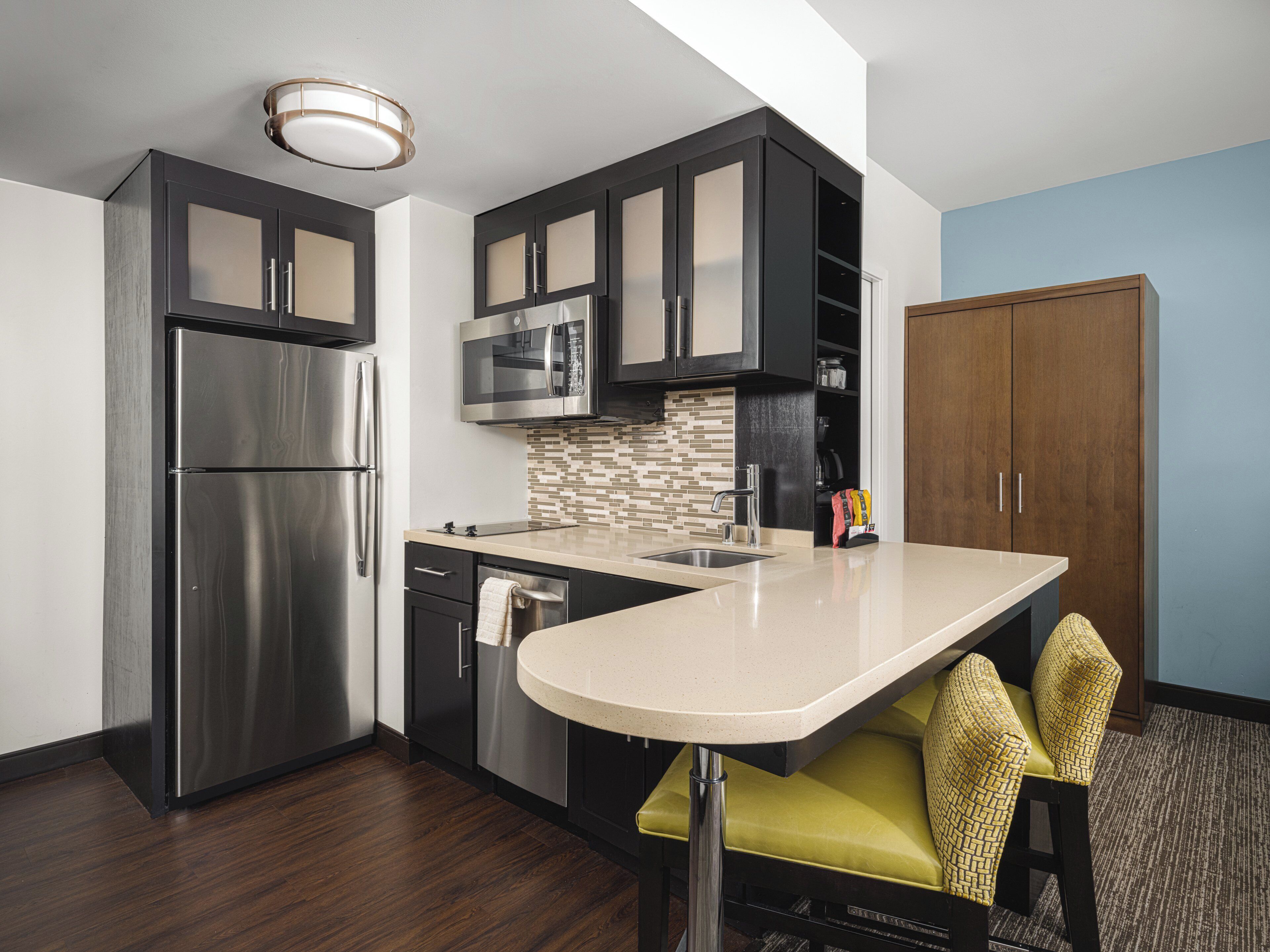 A modern kitchen with a built-in microwave, stainless steel refrigerator, and a small island with a sink.
